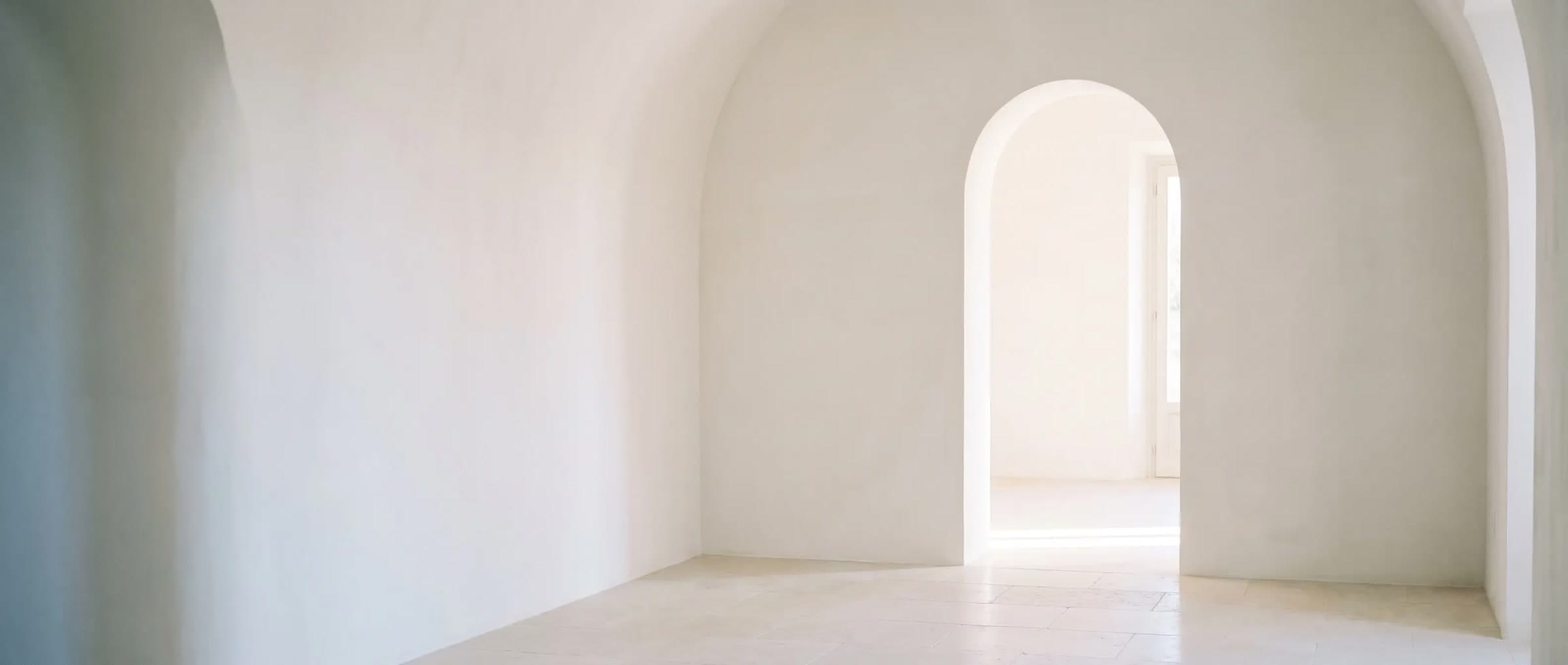 A white plaster room, a tall arched doorway opening onto soft daylight